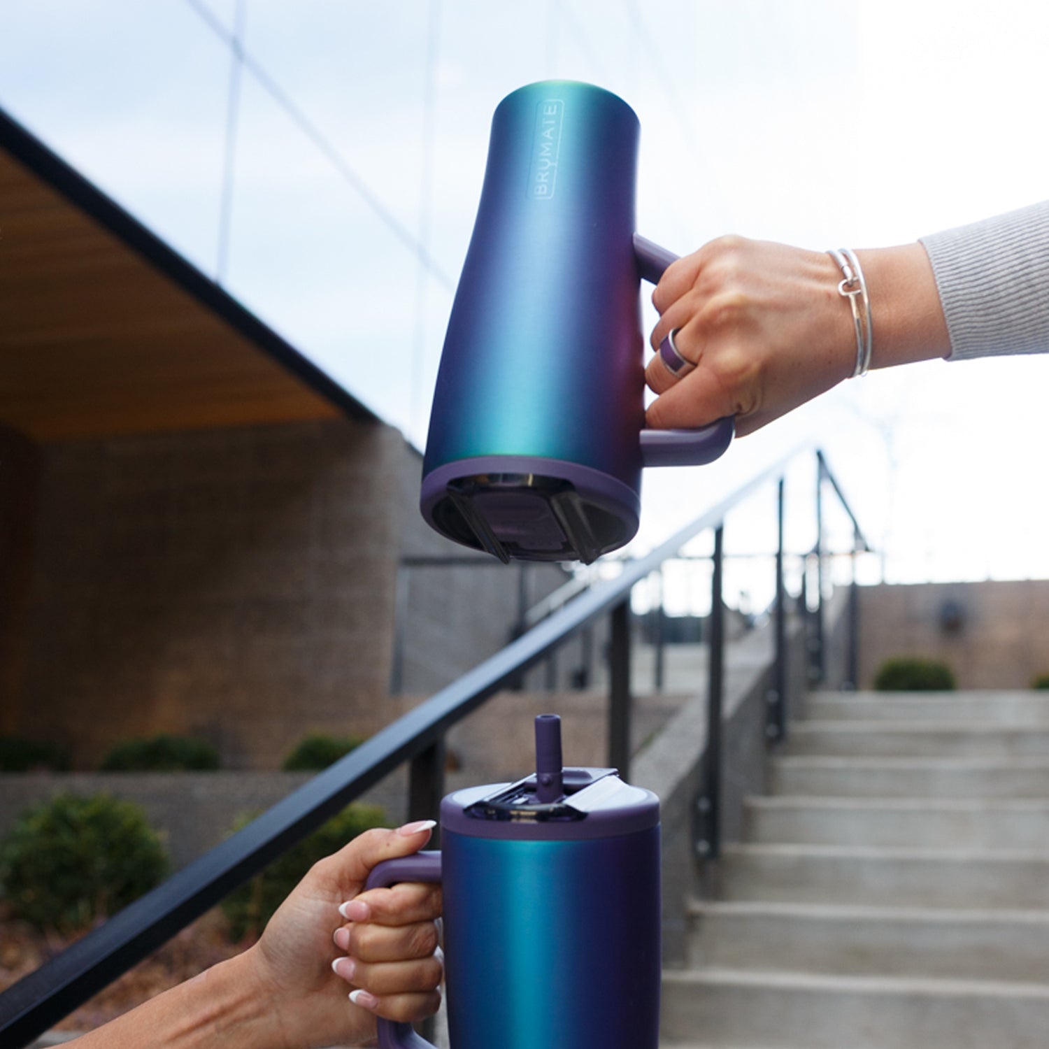 Two hands holding gradient purple Era Flip 30oz tumblers outdoors.