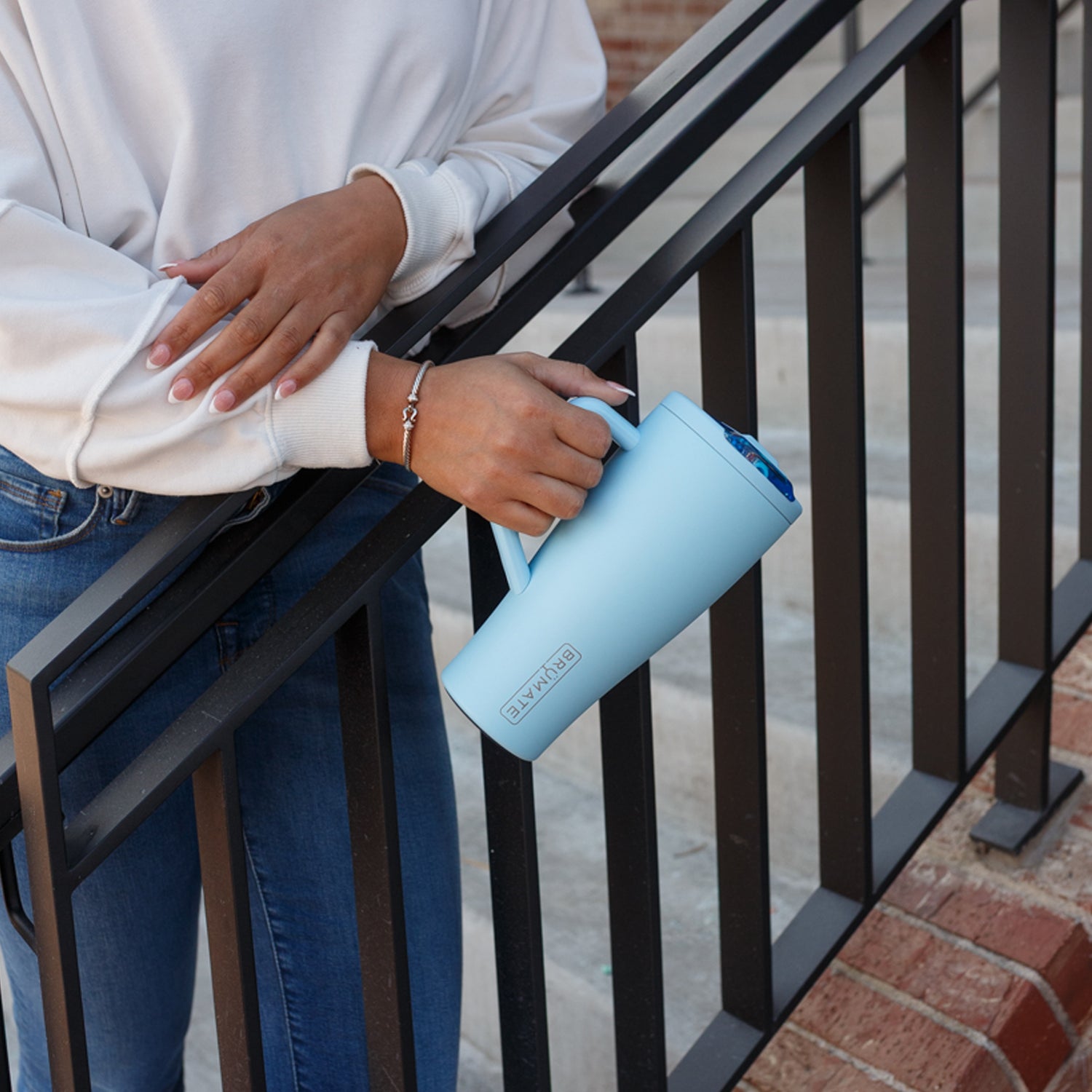 Person holding a light blue Era Flip 30oz tumbler with a black metal railing in the background