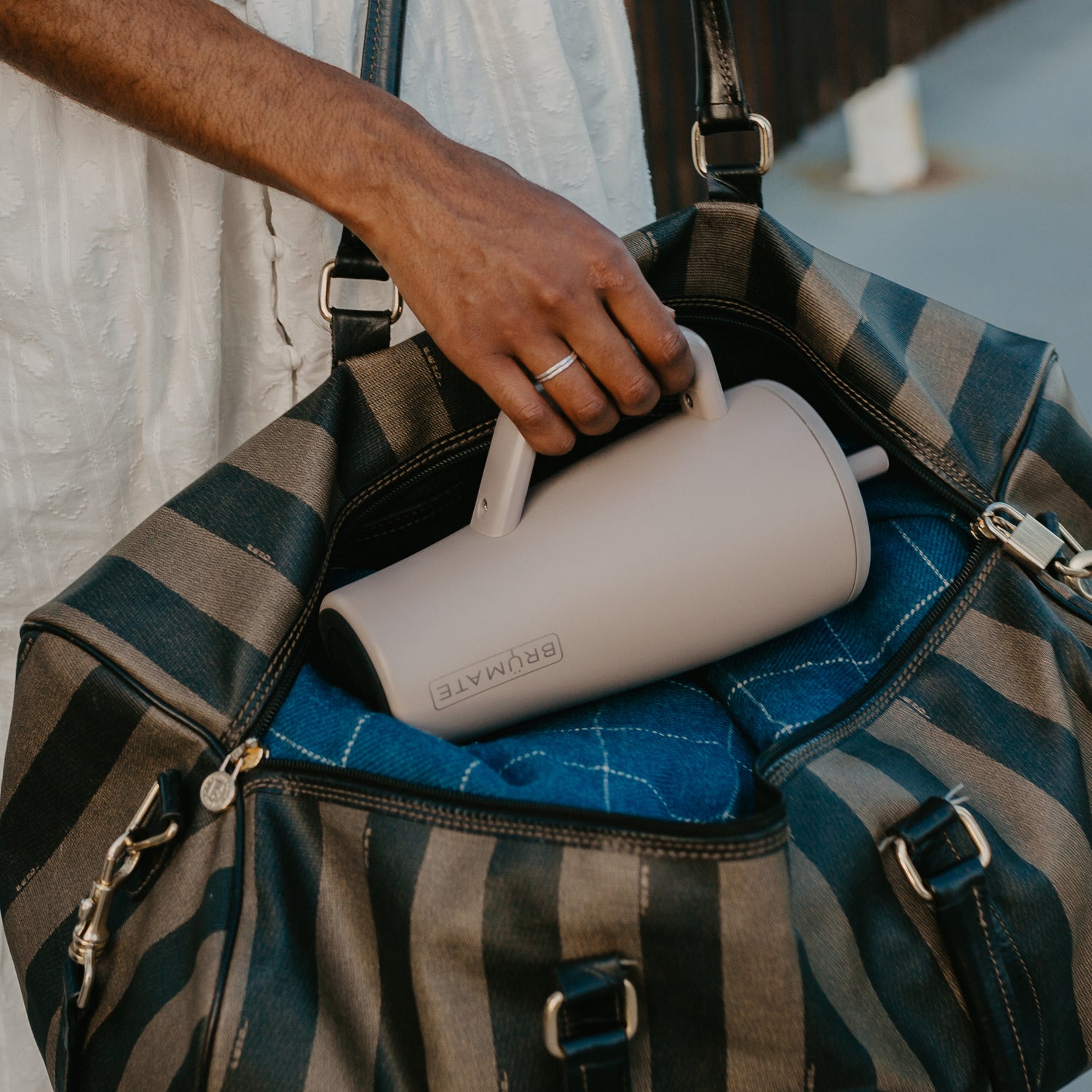 Person placing a beige Era 30oz tumbler into a striped duffel bag.