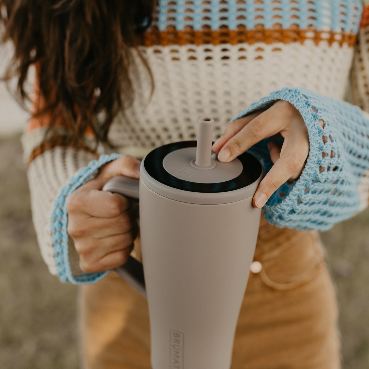Person holding a beige Era 30oz tumbler with a straw lid, wearing a blue knit sleeve.