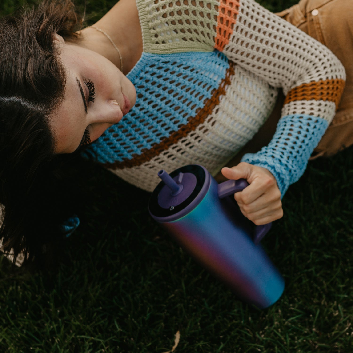 Person lying on grass holding a gradient purple Era 40oz tumbler