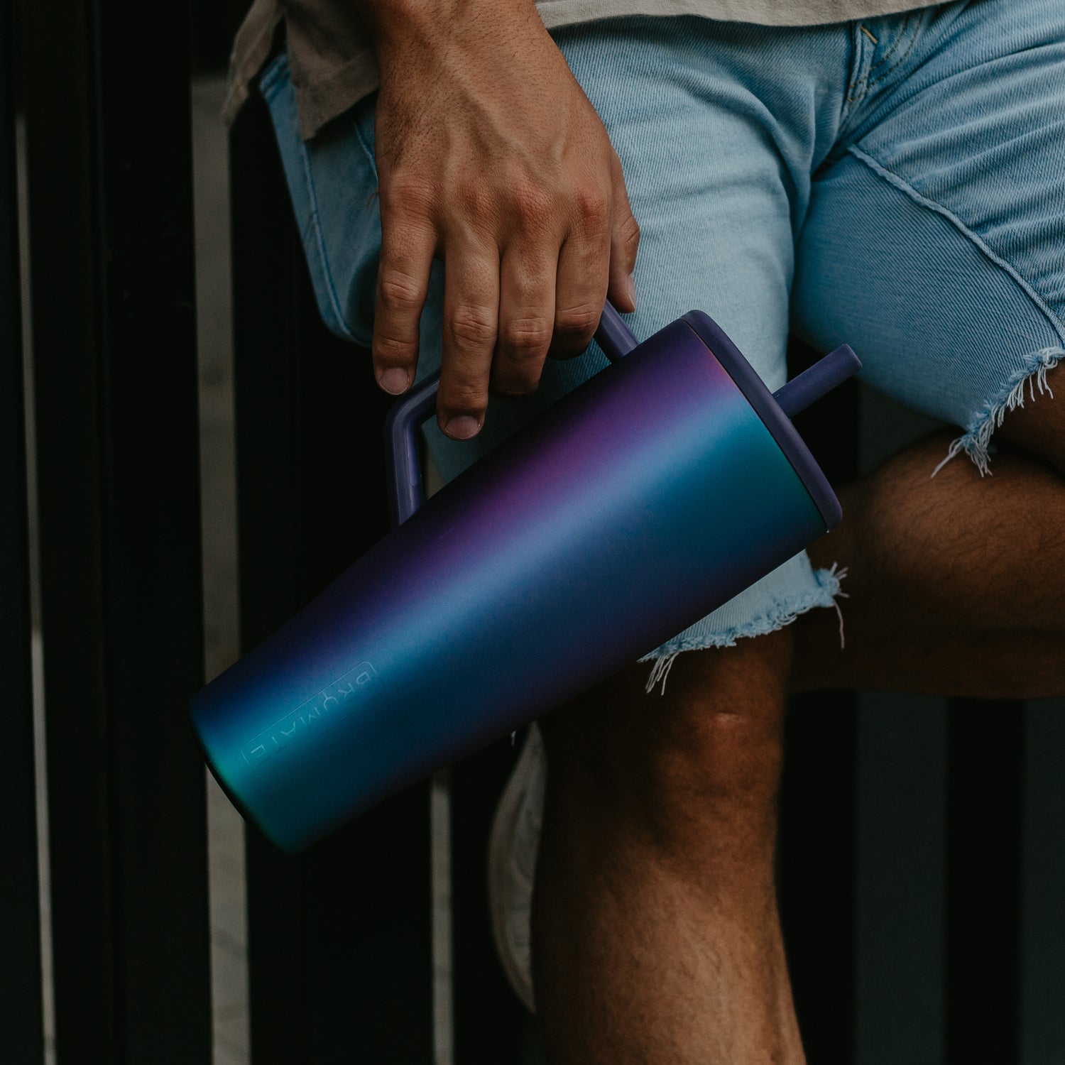 Person holding a gradient purple tumbler with a dark background