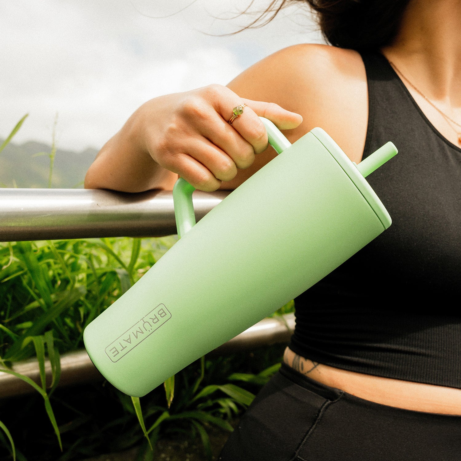 Person holding a green Era 40oz tumbler with a straw outdoors