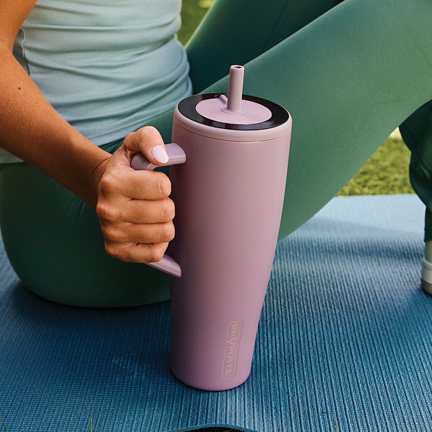 Person holding a purple Era 40oz tumbler with a straw lid on a blue mat outdoors.