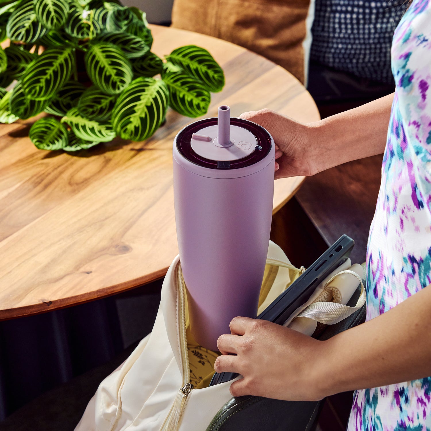 Person holding a purple Era 40oz tumbler with a straw, sitting at a table with plants in the background