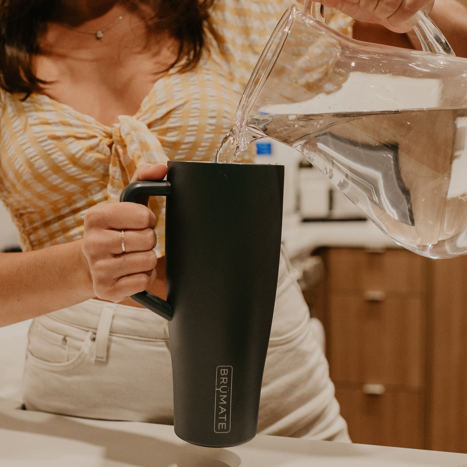 Person pouring water from a clear pitcher into a black BruMate Era 40oz tumbler