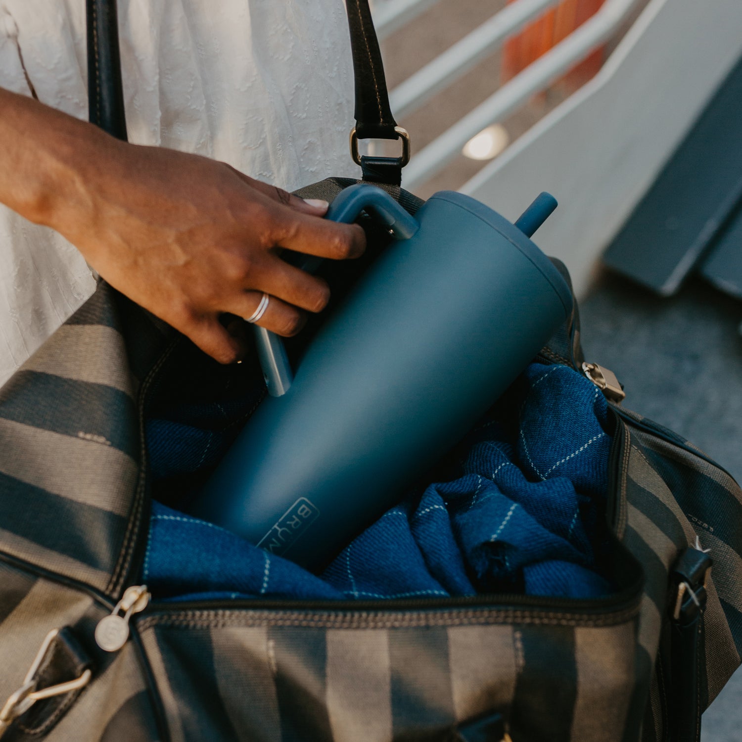 Person placing a blue Era 40oz tumbler into a striped bag