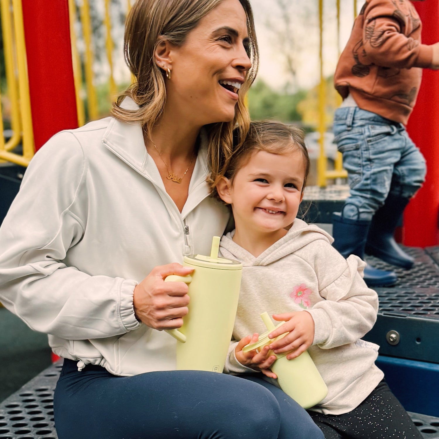 Woman and child sitting on a playground, holding yellow Era 40oz and Leap 12oz tumblers.