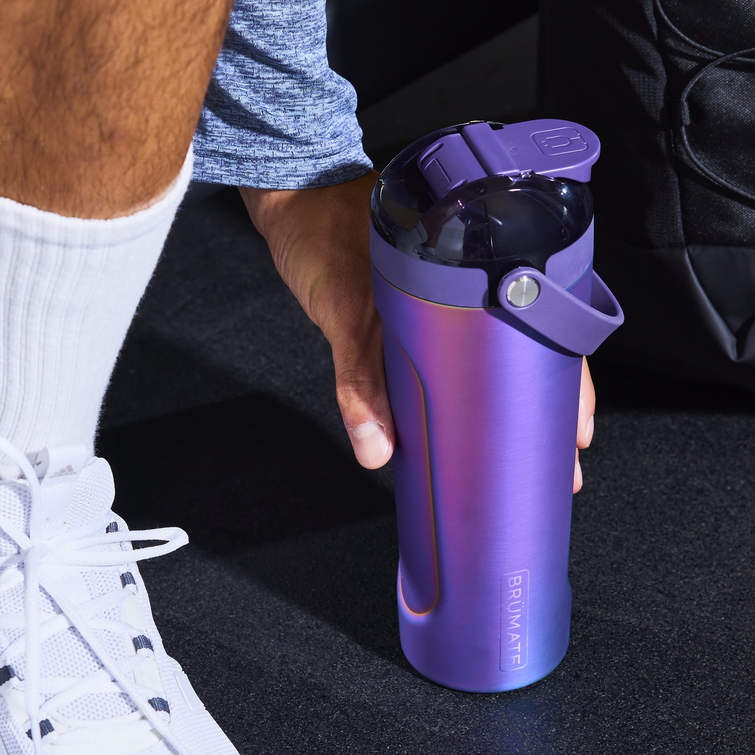 Gradient purple MultiShaker 25oz Fitness Shaker held by a person with white sneakers on a dark surface