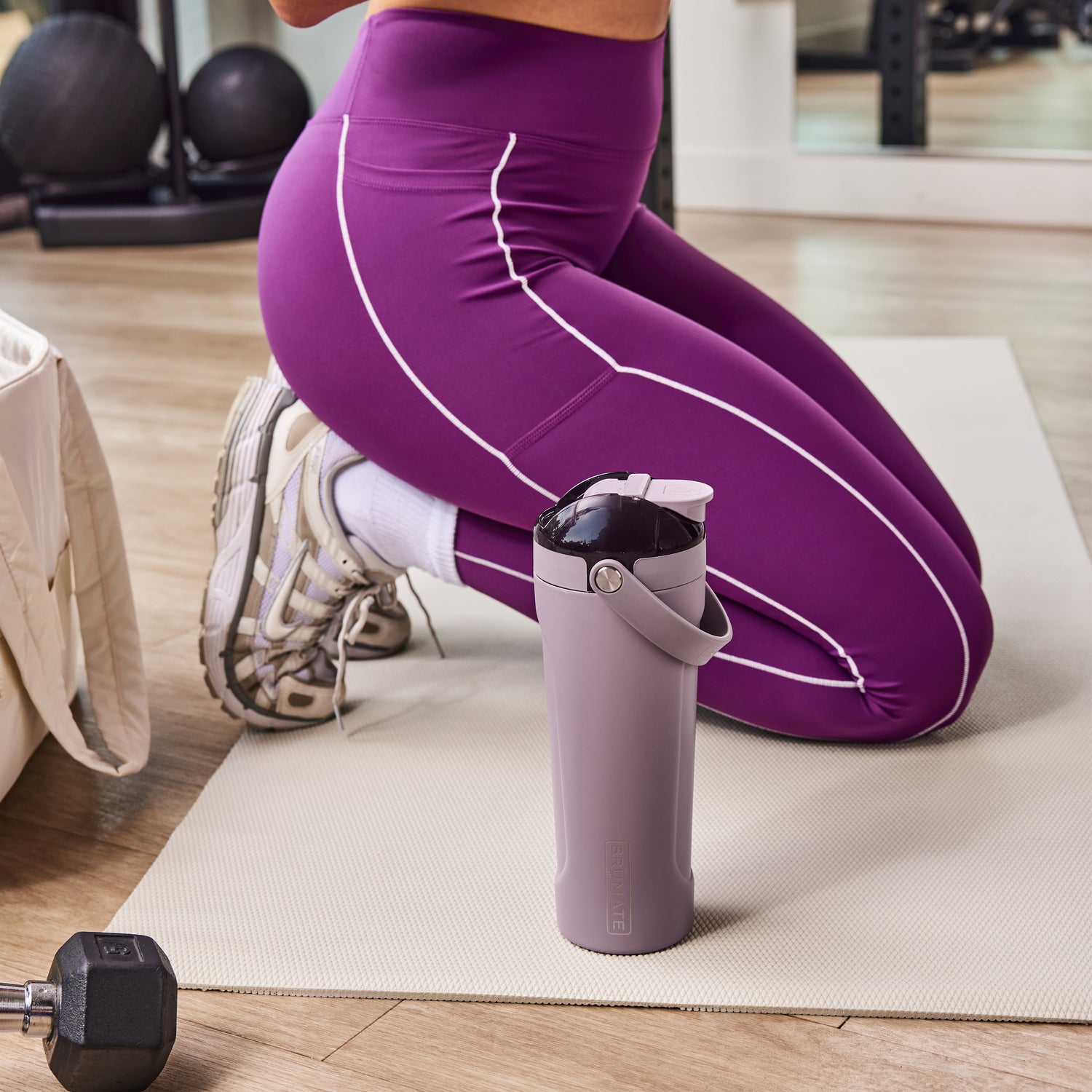 Person in purple leggings exercising on a mat with a purple MultiShaker 25oz Fitness Shaker nearby.