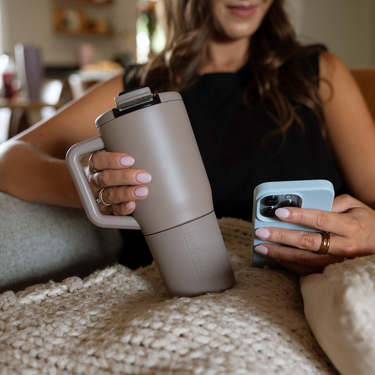 Person holding a beige Muv 25oz mug and a phone in a casual setting