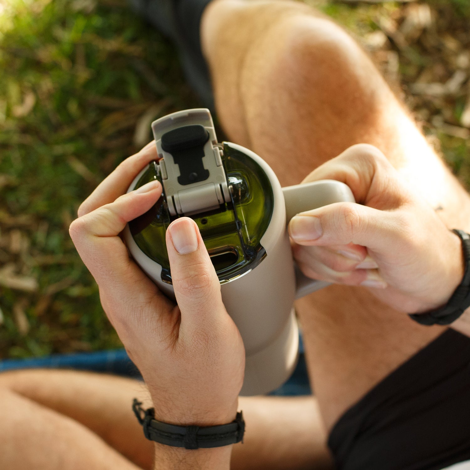 Person holding a beige Muv 25oz mug with a green interior, sitting outdoors.