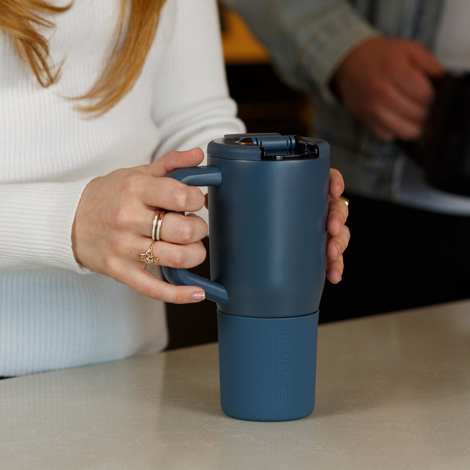 Person holding a blue Muv 25oz mug with a blurred background