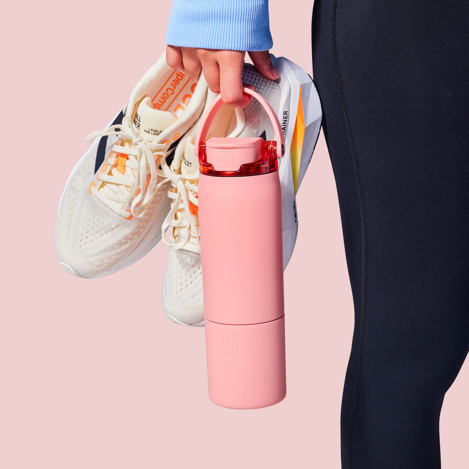 Person holding a pink Rise 25oz water bottle with white sneakers on a pink background