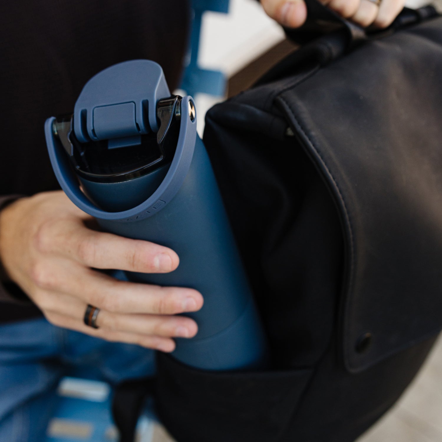 Person holding a blue Rise 25oz water bottle with a black backpack
