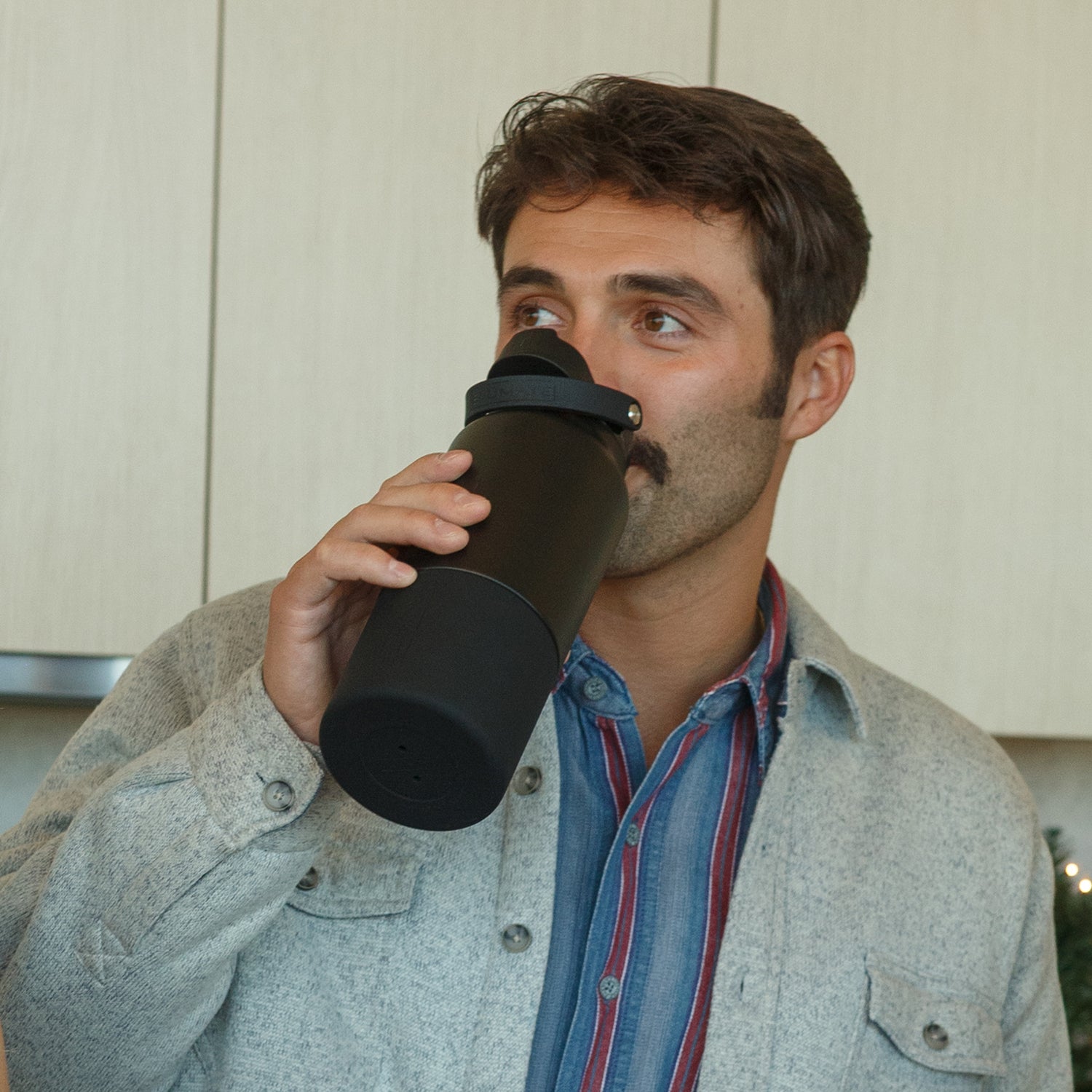 Man drinking from a black Rise 35oz water bottle in a kitchen setting