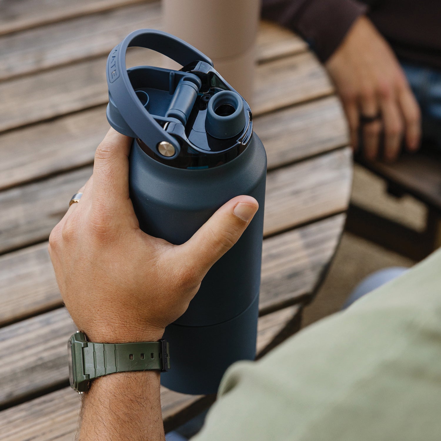 Person holding a blue Rise 35oz water bottle on a wooden surface