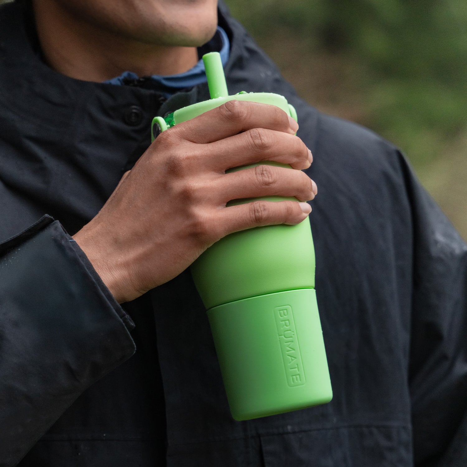 Person holding a green Resa 25oz tumbler with a straw lid, wearing a dark jacket.