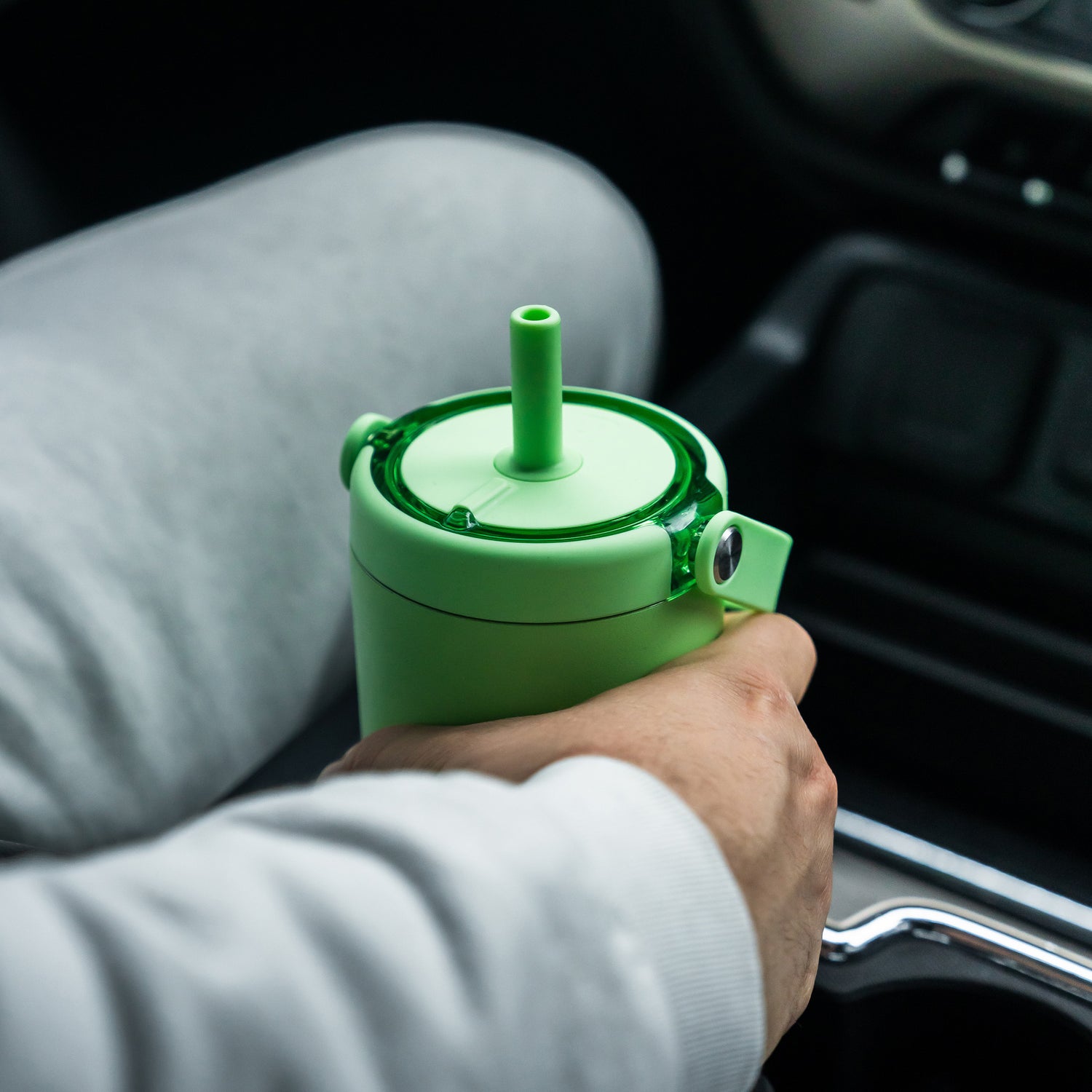 Person holding a green Resa 25oz tumbler with a straw in a car.