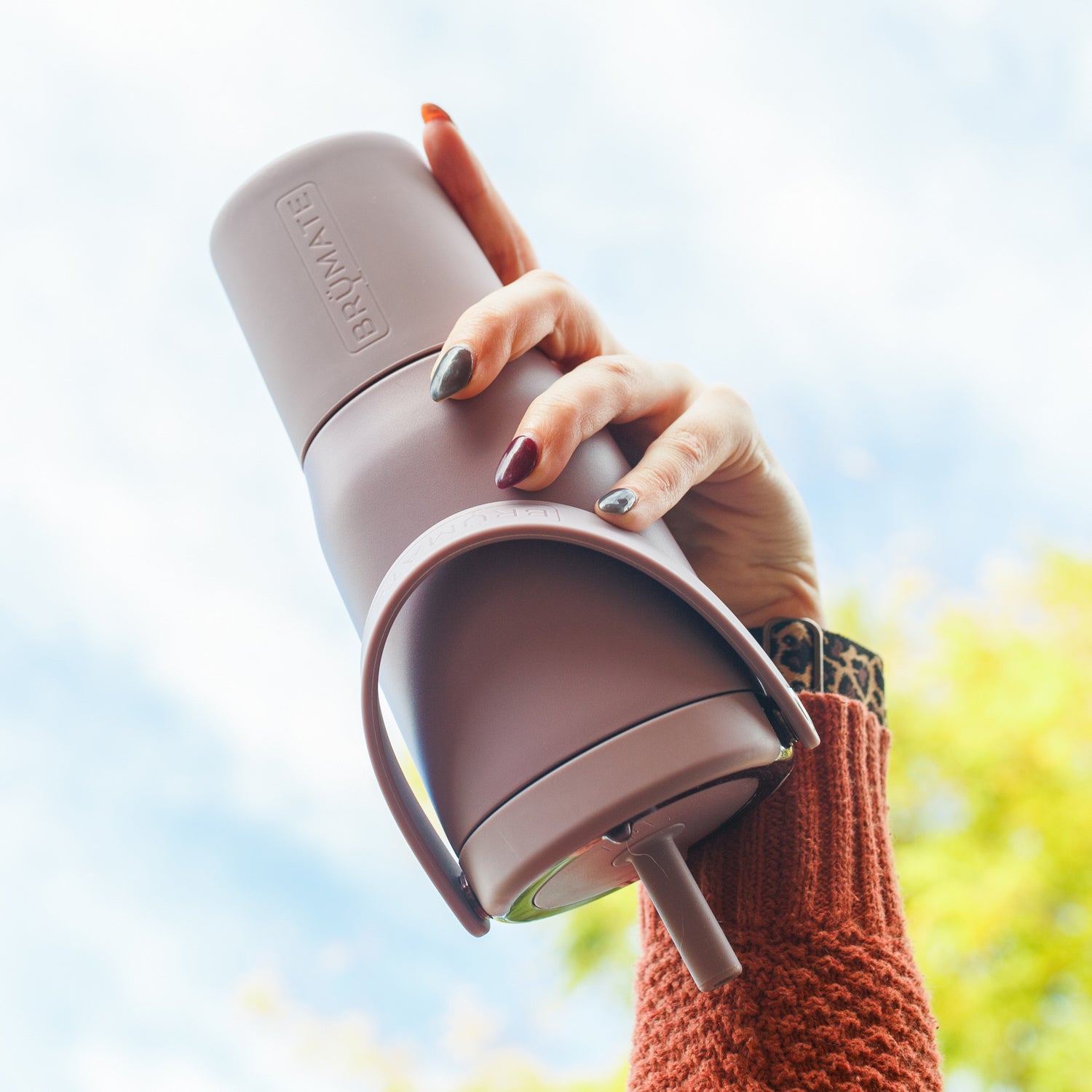Person holding a purple Resa 25oz tumbler with a blurred outdoor background