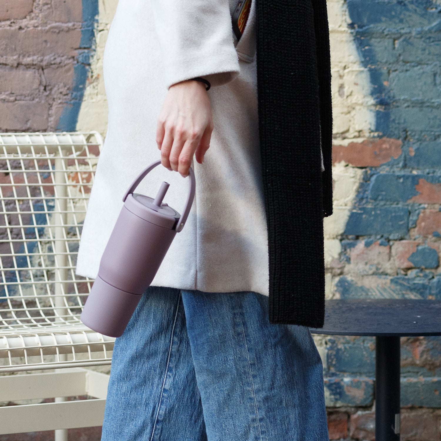 Person holding a purple Resa 25oz tumbler against a textured wall background