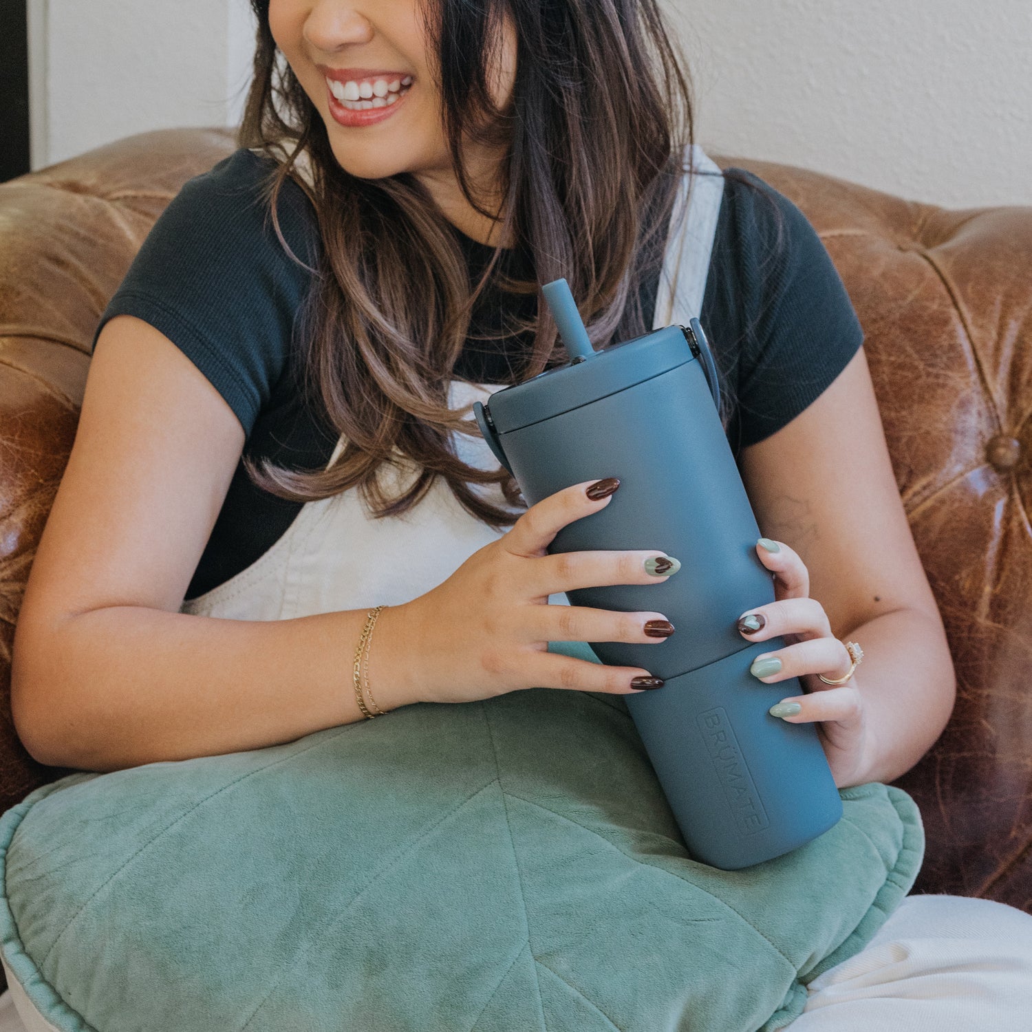 Woman holding a blue Resa 35oz tumbler with a straw on a brown couch.