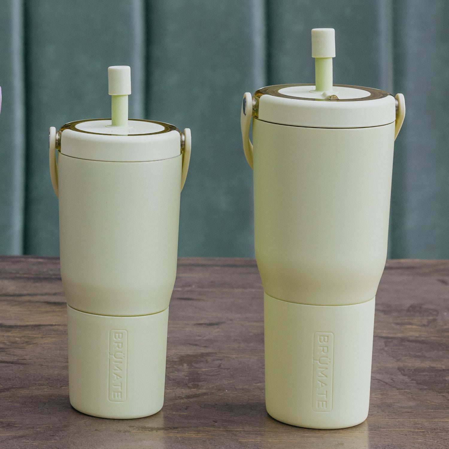 Two yellow Resa tumblers on a wooden surface against a green metal background