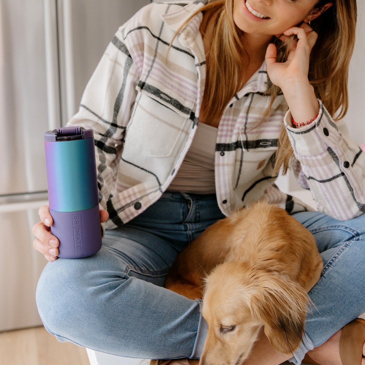 Woman holding a gradient purple Strova 18oz coffee tumbler with a dog on her lap indoors.