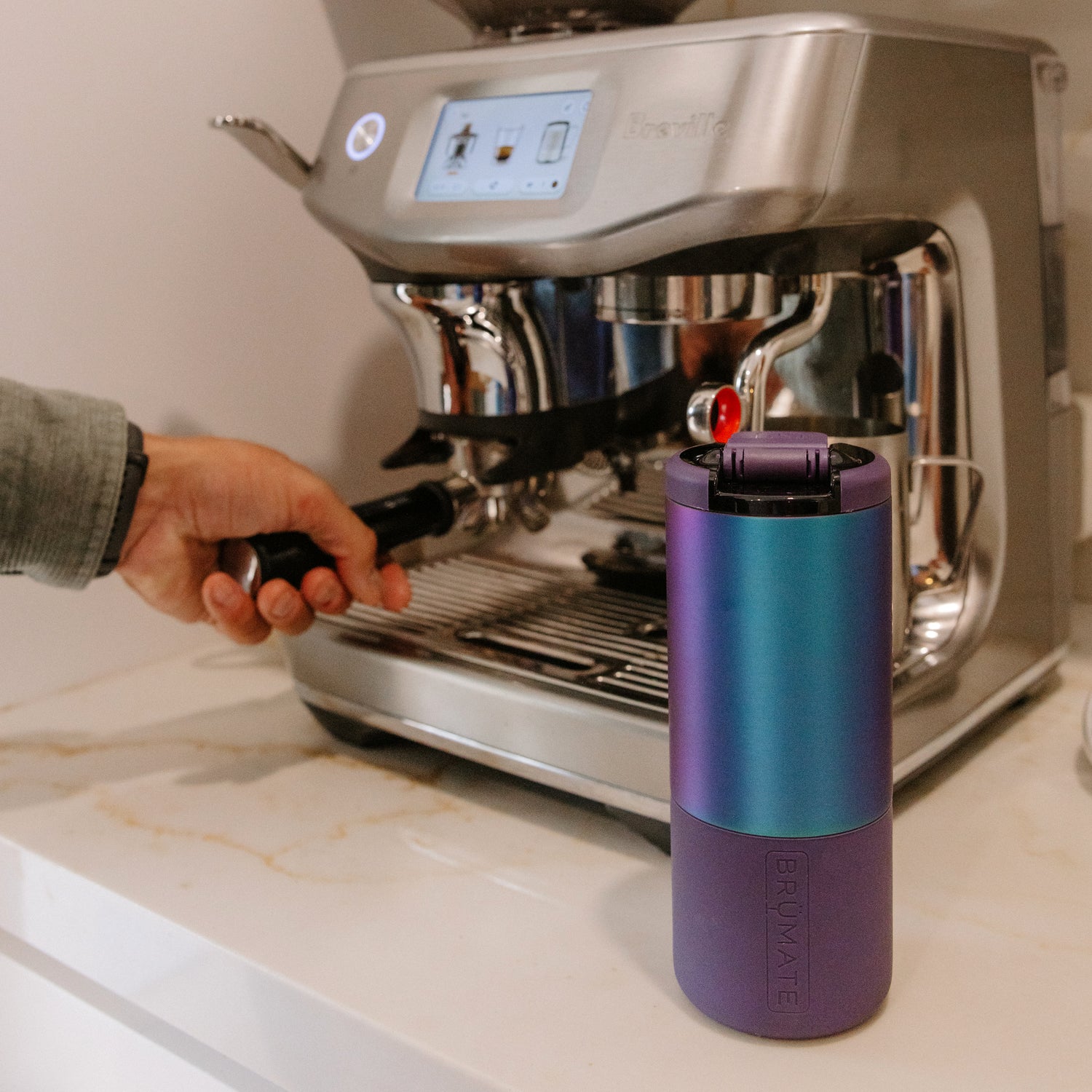 Person using a gradient purple Strova 18oz coffee tumbler with an espresso machine in the background