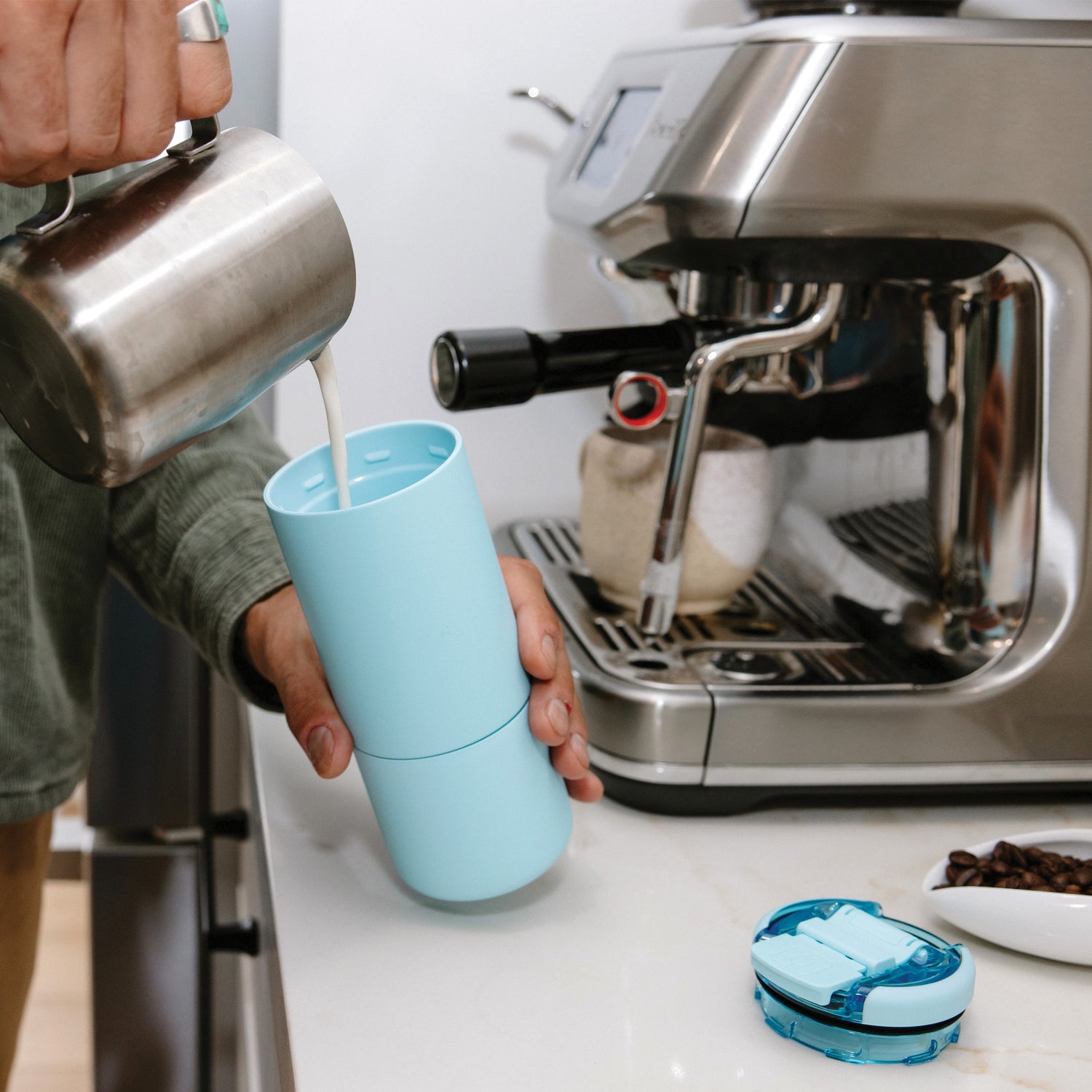 Person pouring milk into a blue Strova 18oz coffee tumbler next to an espresso machine.
