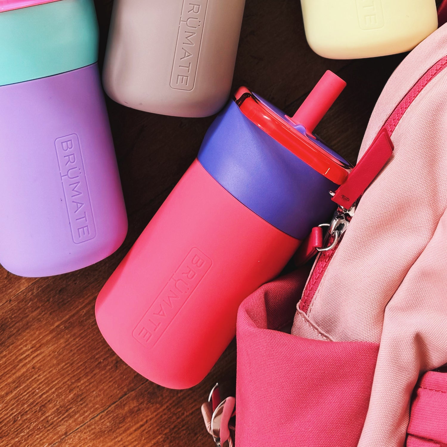 Colourful BruMate Leap 12oz tumblers on a wooden surface with a pink bag.