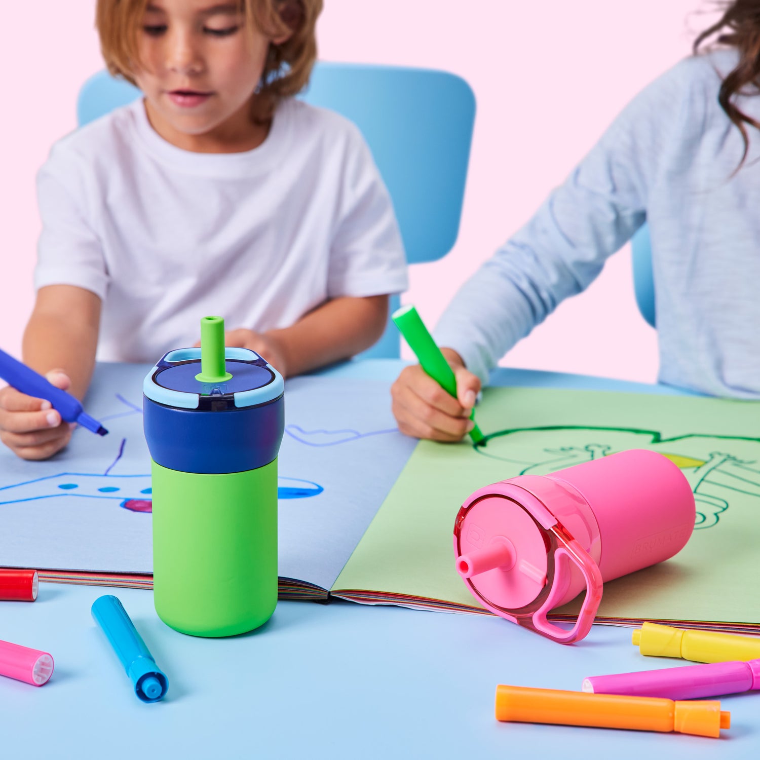 Two children drawing with markers at a table, surrounded by colourful Leap 12oz tumblers and markers.