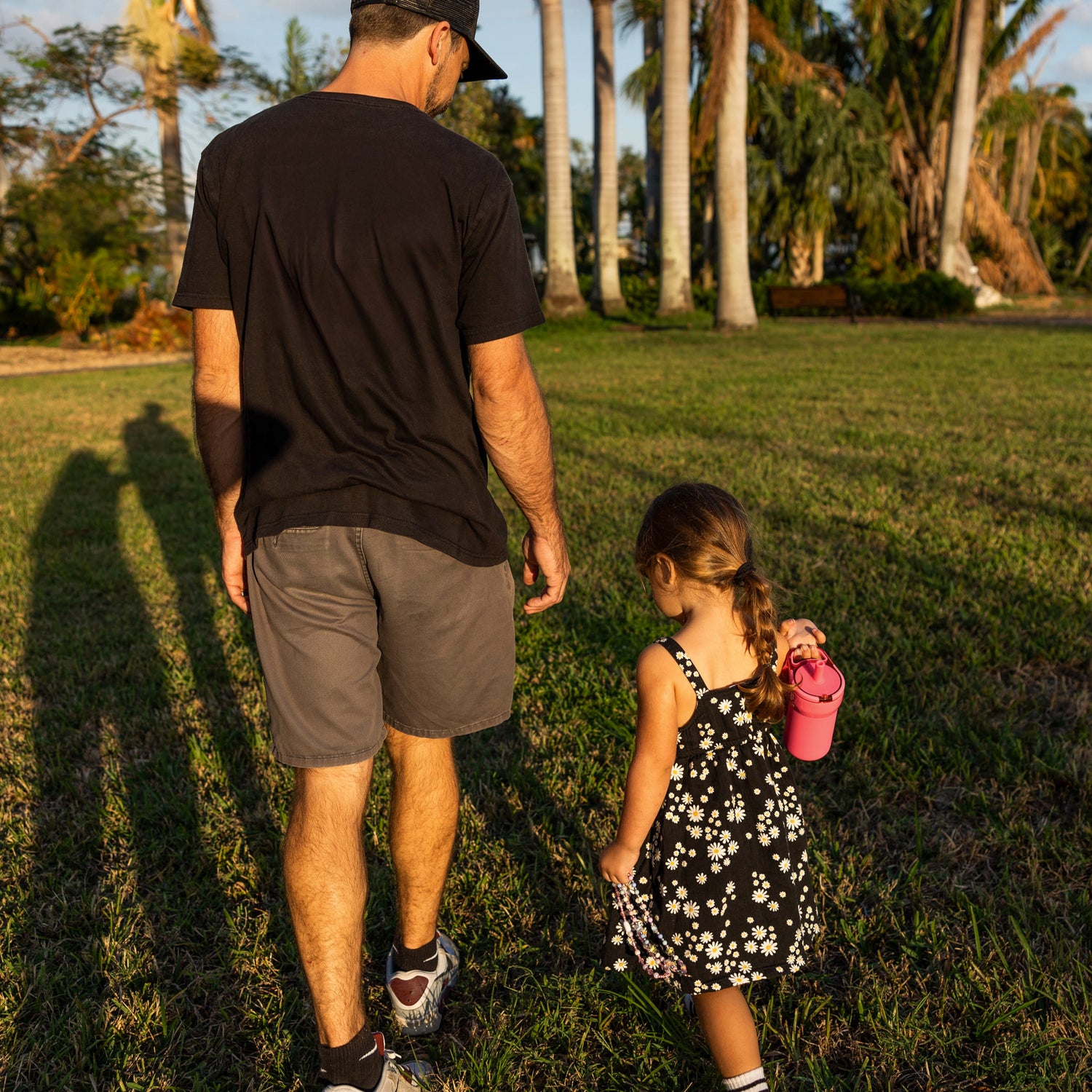 Man and young girl walking with bright pink Leap 12oz tumbler together in a park with palm trees in the background