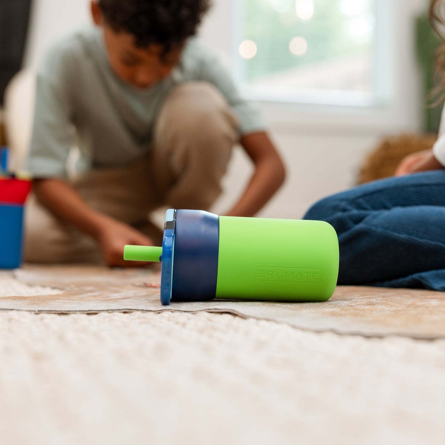 Green and blue Leap 12oz tumbler on a wooden floor with children playing in the background