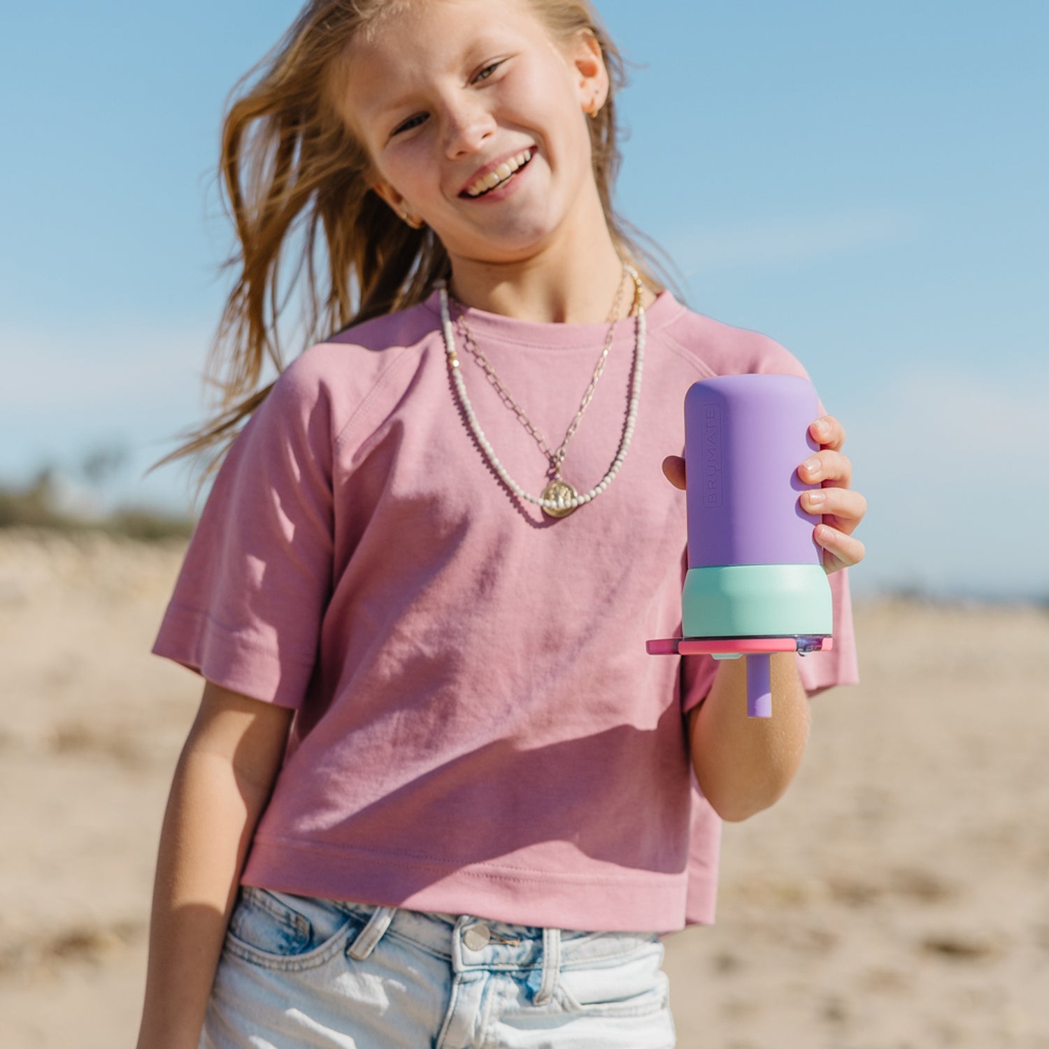 Young girl holding a purple and pink Leap 12oz tumbler on a beach