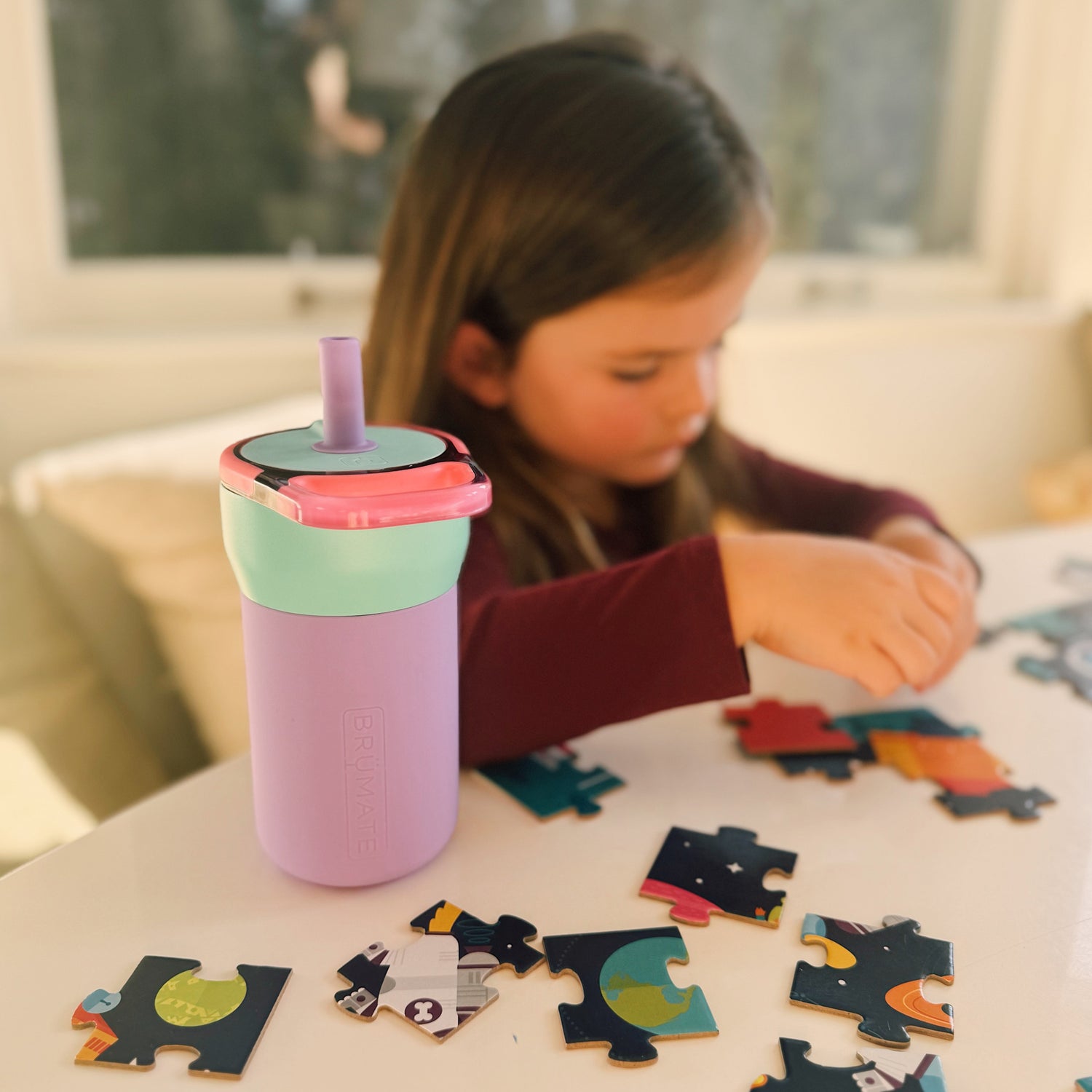 Child playing with a puzzle and a colourful purple and green Leap 12oz tumbler on a table.