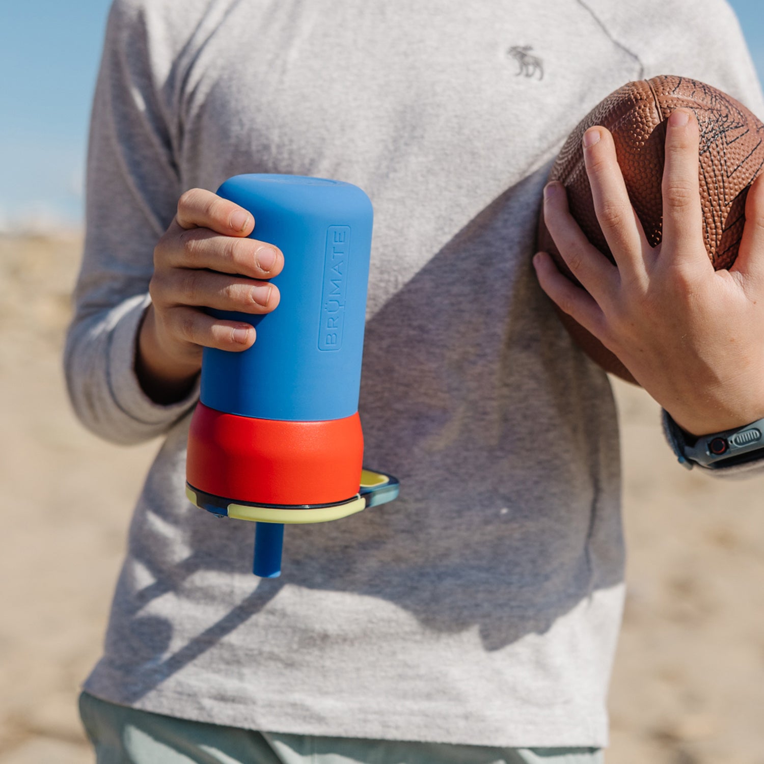 Person holding a blue and red Leap 12oz tumbler and a ball outdoors.